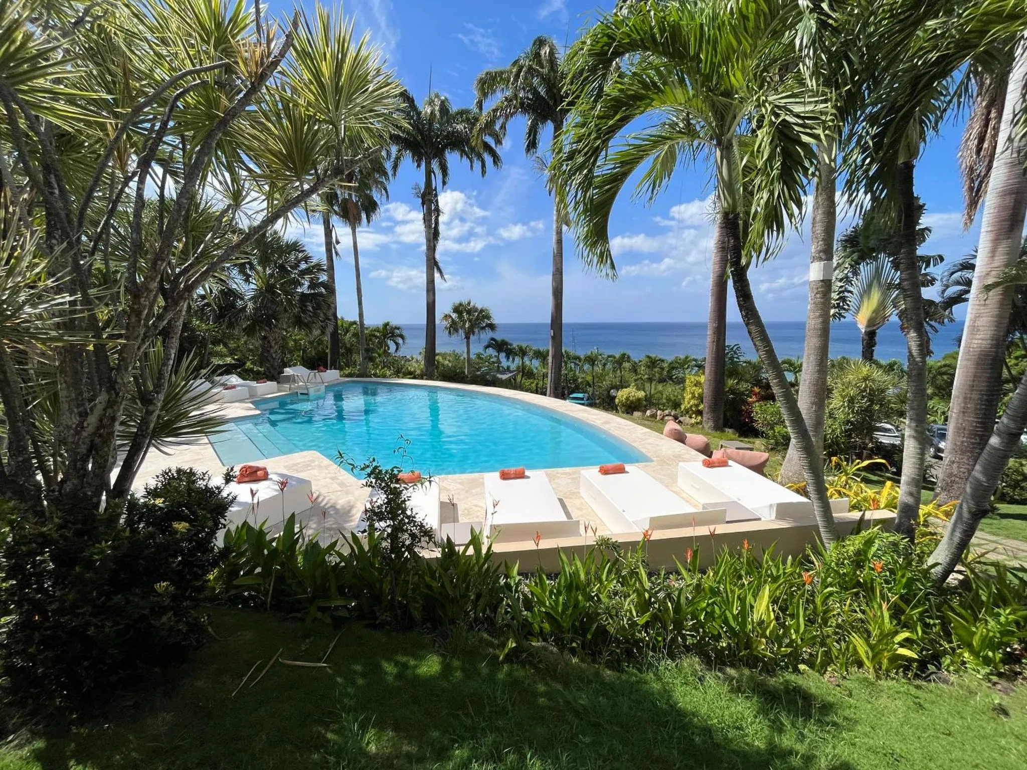 Une piscine bordée de transats blancs et de végétation luxuriante offre une vue sur la mer.