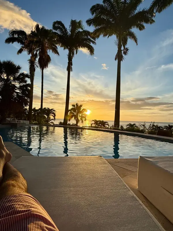 Une piscine à débordement reflète le coucher de soleil sur l'océan, avec des palmiers en arrière-plan.