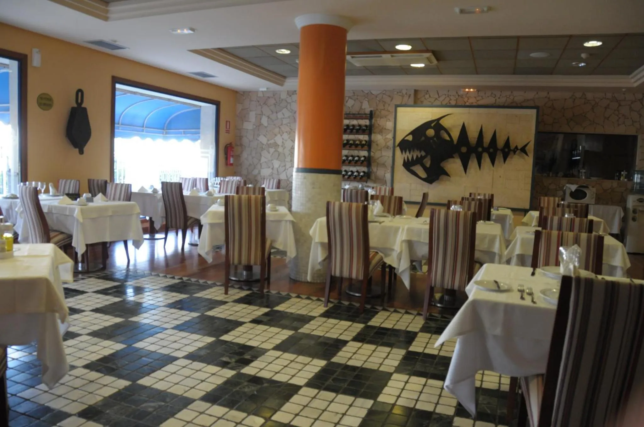 Une salle de restaurant lumineuse avec des tables dressées et un sol à carreaux.
