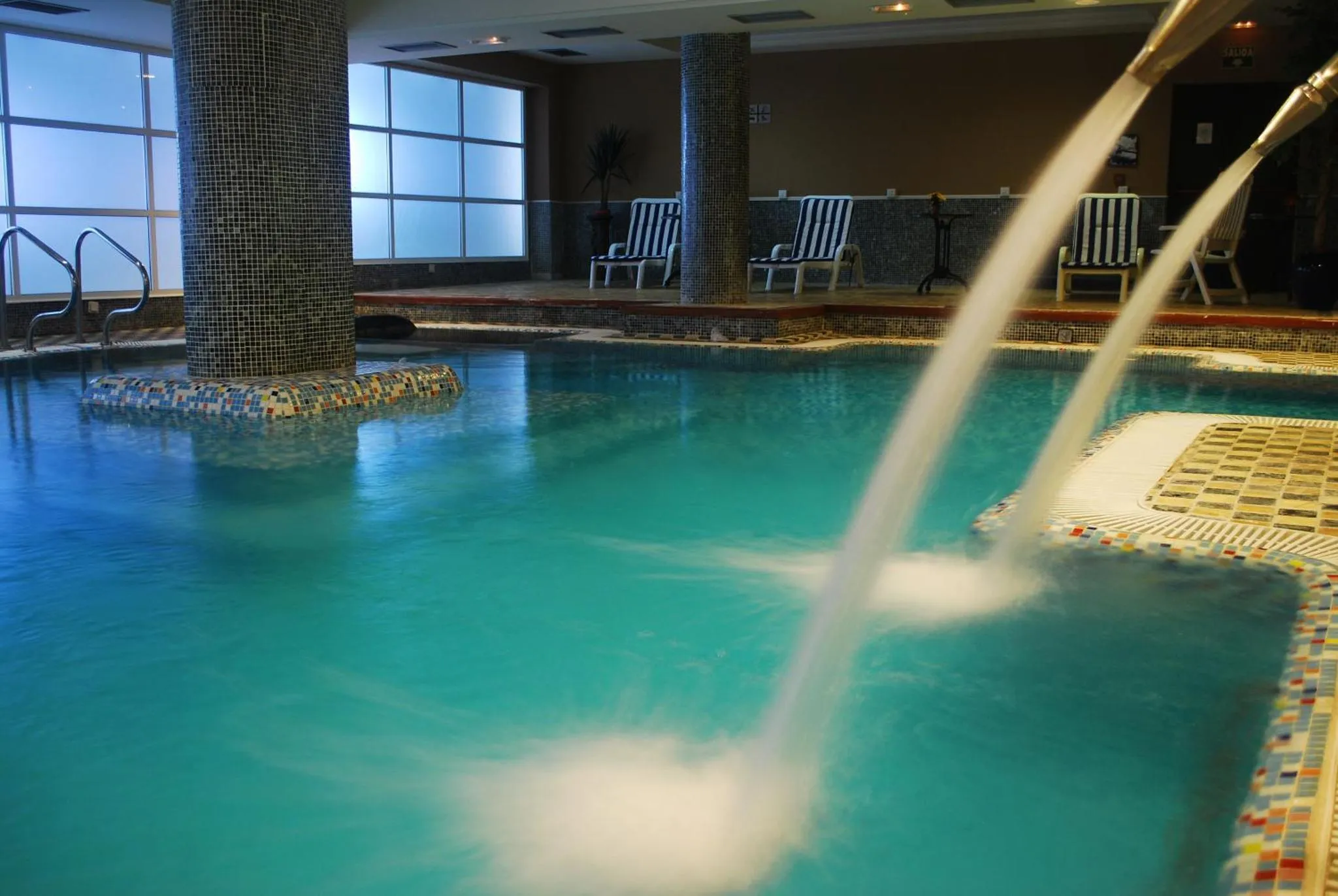 Une piscine intérieure avec un jet d'eau et des chaises longues sur le bord.