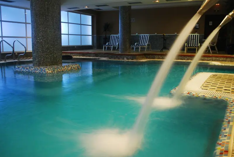 Une piscine intérieure avec un jet d'eau et des chaises longues sur le bord.