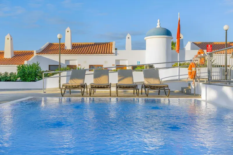 Transats alignés au bord d'une piscine turquoise avec un bâtiment blanc en arrière-plan.