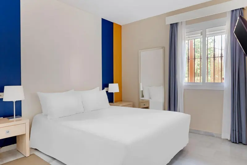 Une chambre lumineuse avec un grand lit blanc et des tables de chevet.