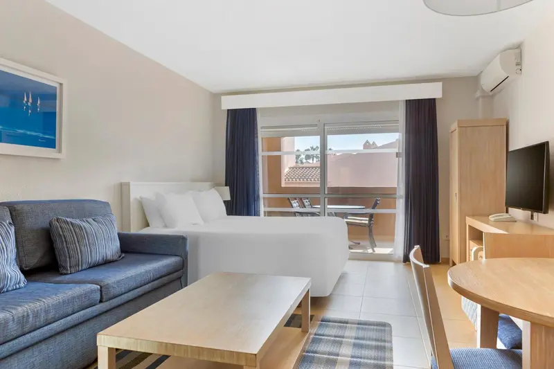 Une chambre lumineuse avec un canapé, un lit et un accès à un balcon.