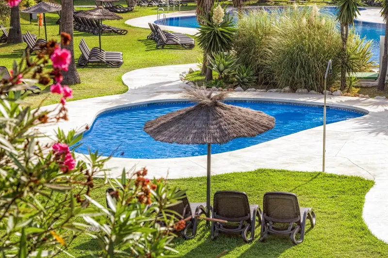 Transats et parasols ombragent une piscine au milieu d'une pelouse verdoyante.