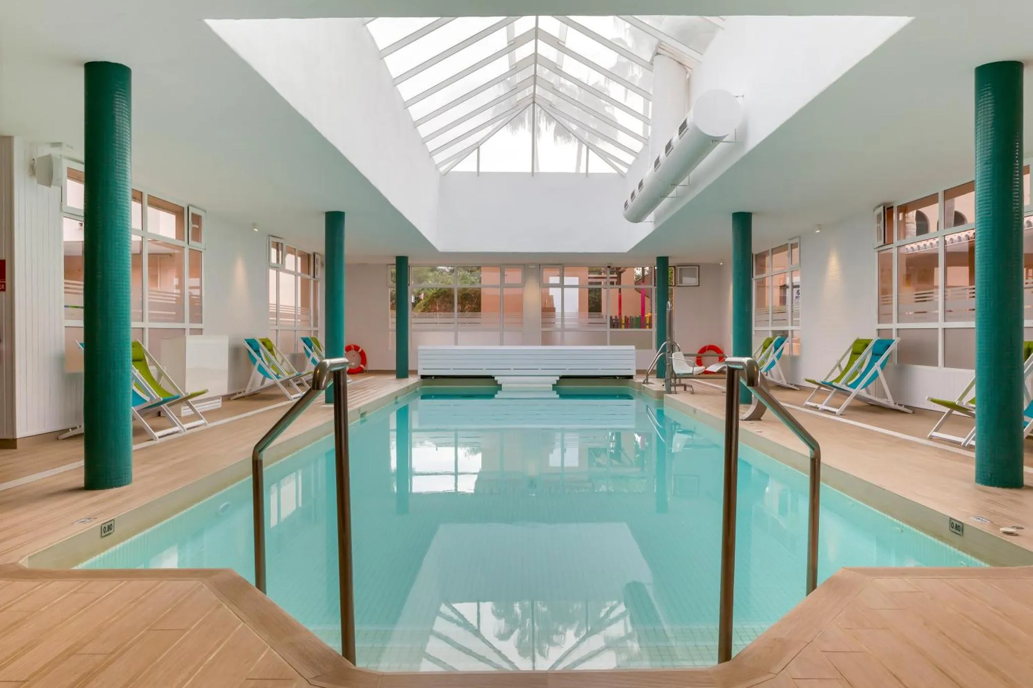 Une piscine intérieure lumineuse avec des transats bleus et verts.
