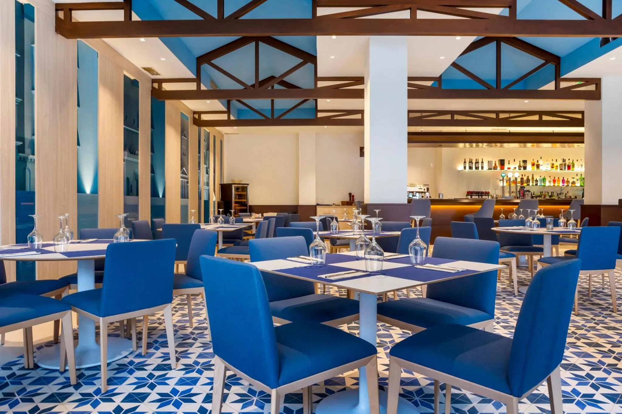Une salle de restaurant lumineuse avec des tables dressées et un comptoir de bar.