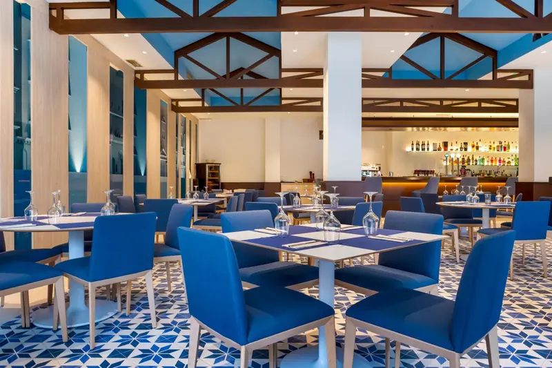 Une salle de restaurant lumineuse avec des tables dressées et un comptoir de bar.