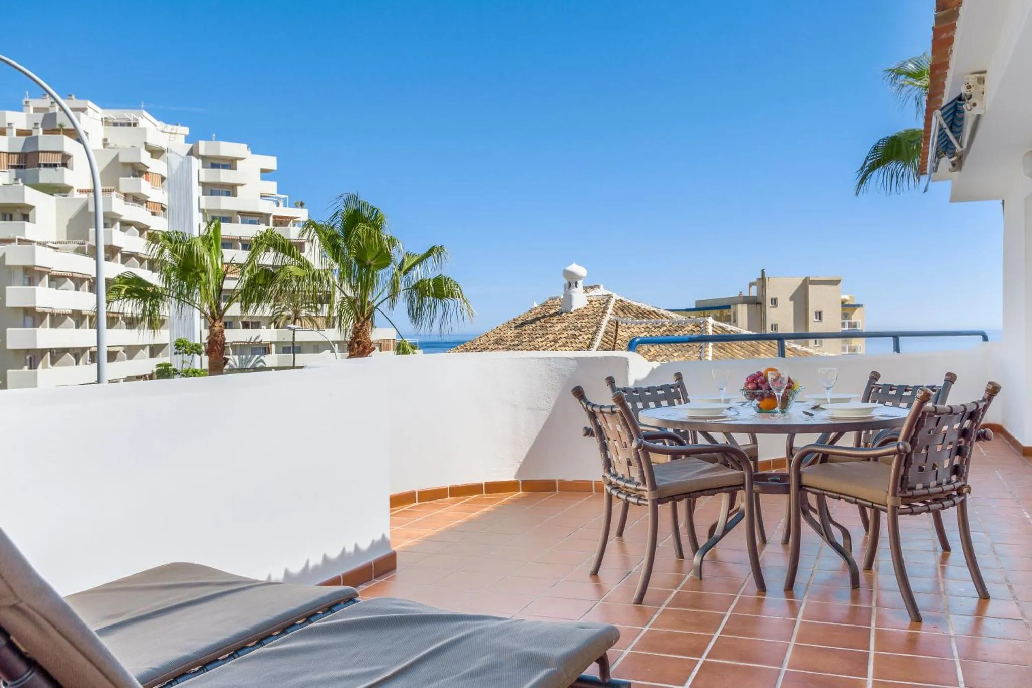 Une table et des chaises sont disposées sur une terrasse ensoleillée avec vue sur la mer.