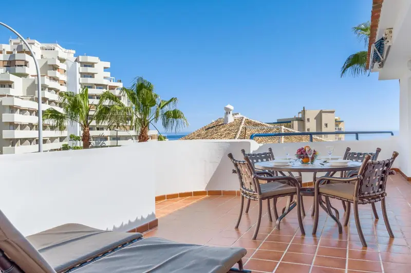 Une table et des chaises sont disposées sur une terrasse ensoleillée avec vue sur la mer.