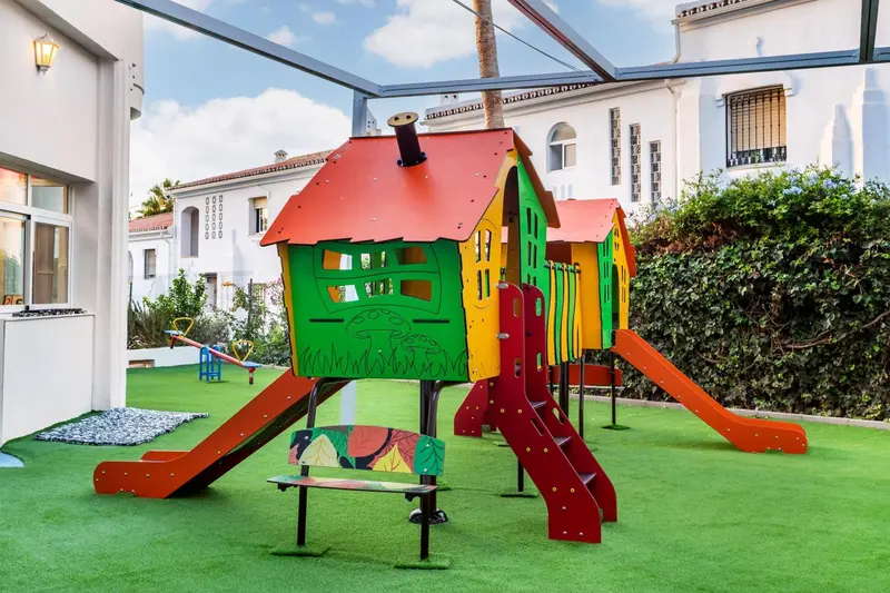 Structure de jeu colorée sur une pelouse verte dans une cour intérieure.