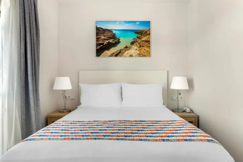 Une chambre lumineuse avec un grand lit et une décoration murale représentant un paysage marin.
