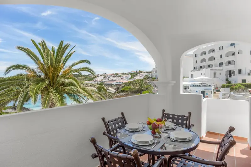 Une table est dressée sur une terrasse avec vue sur la mer et la végétation.