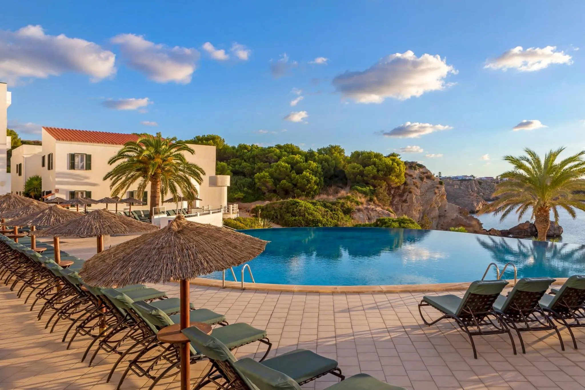 Transats et parasols bordent une piscine à débordement avec vue sur la mer.