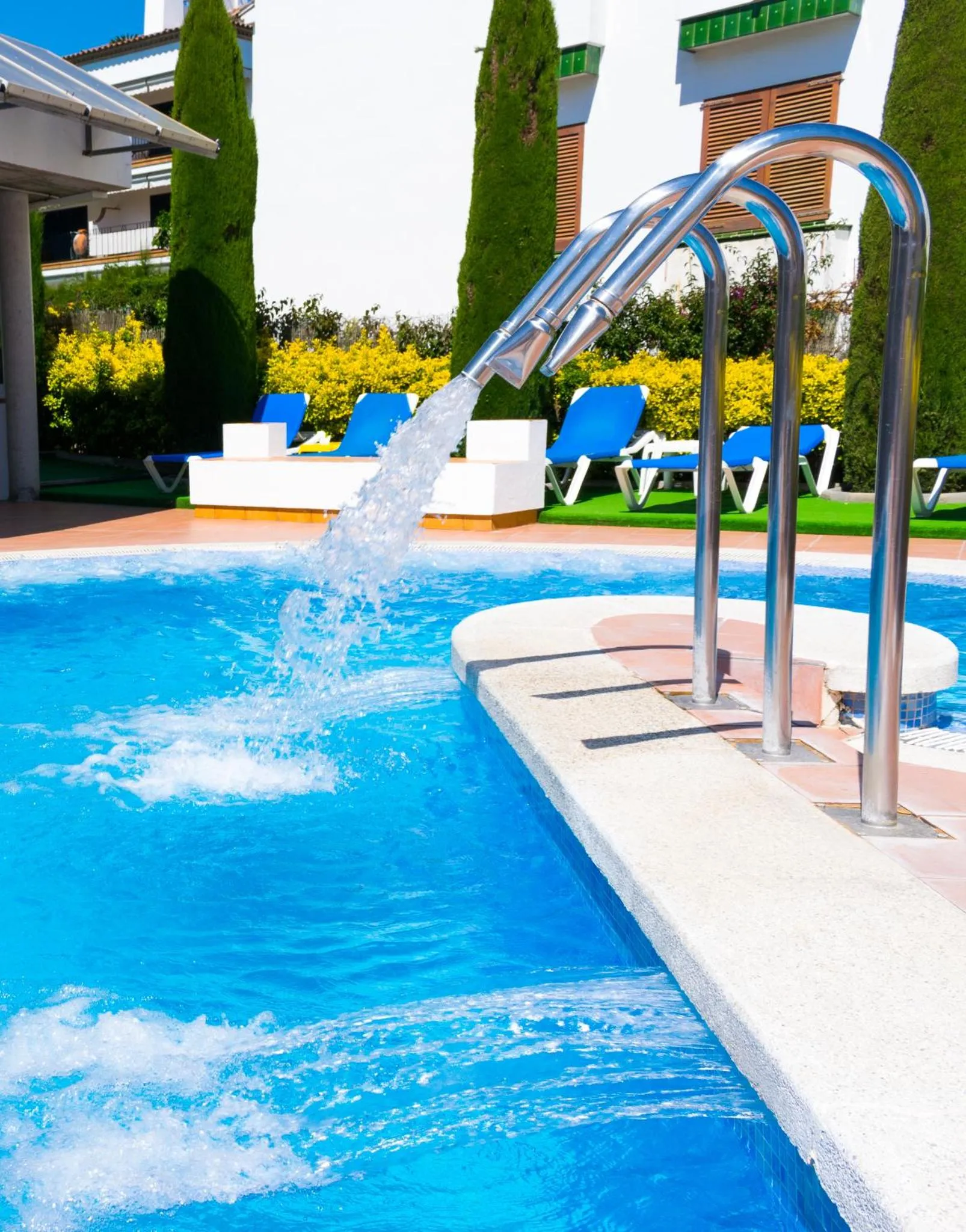 Une piscine avec une cascade et des transats bleus.