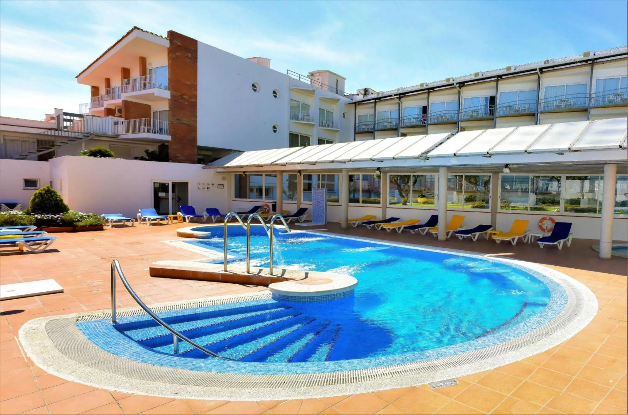 Piscine extérieure avec transats et parasols devant un bâtiment.