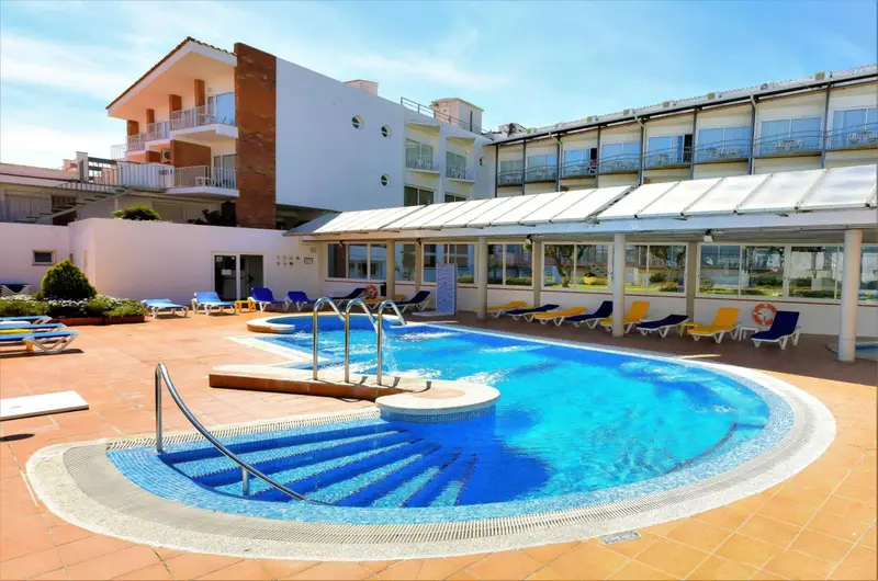 Piscine extérieure avec transats et parasols devant un bâtiment.