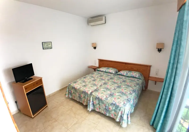 Une chambre lumineuse avec un lit double et un meuble télévision.