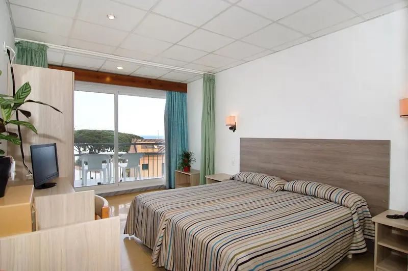 Chambre lumineuse avec un lit double et un balcon donnant sur la mer.