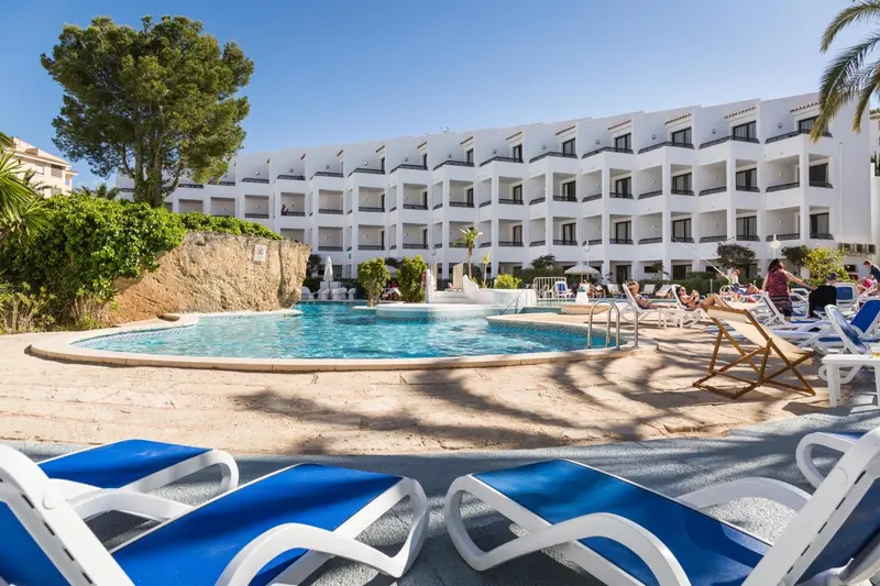 Transats bleus au bord d'une piscine ensoleillée devant un bâtiment blanc.