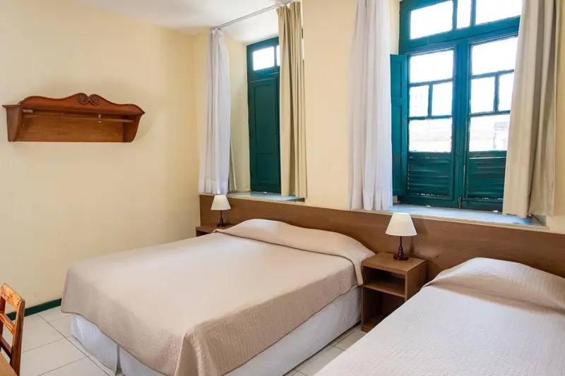 Une chambre lumineuse avec deux lits simples et des rideaux blancs.