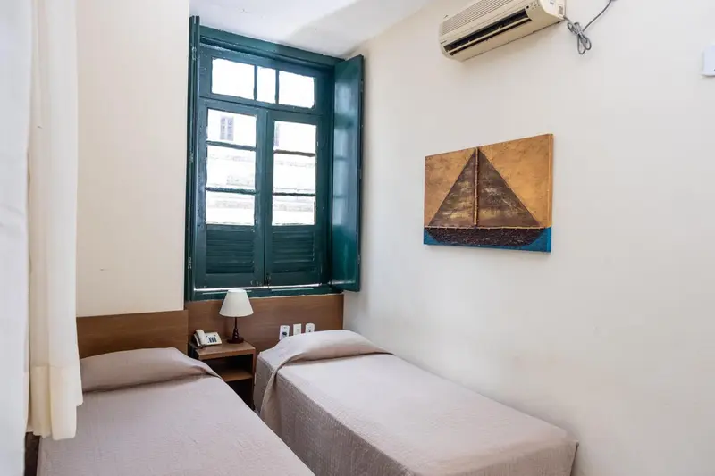 Une chambre lumineuse avec deux lits simples et une fenêtre à volets verts.