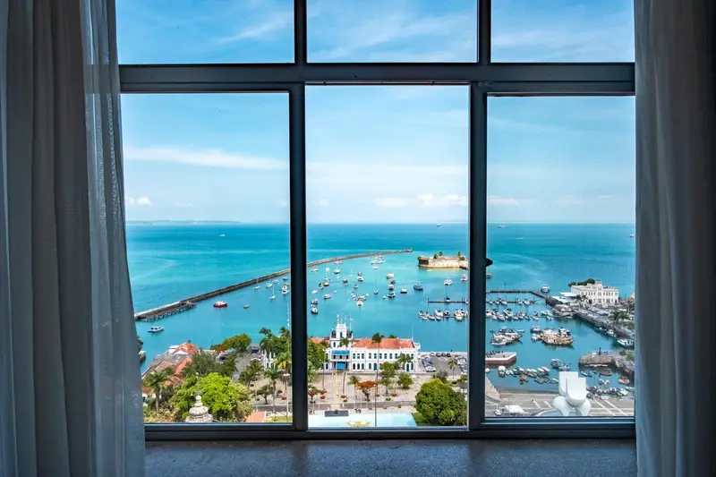 Vue panoramique sur la mer et un port depuis une fenêtre.