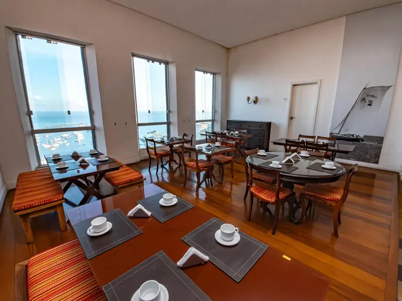 Une salle lumineuse avec des tables dressées pour le petit-déjeuner face à la mer.