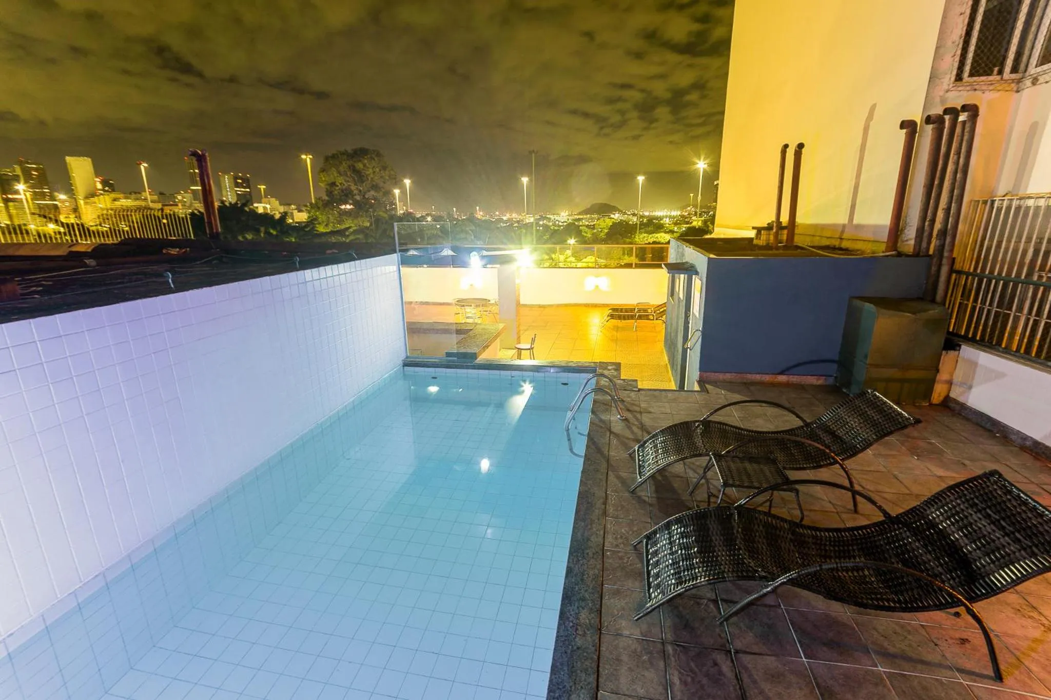 Une piscine rectangulaire avec des transats sur une terrasse illuminée la nuit.