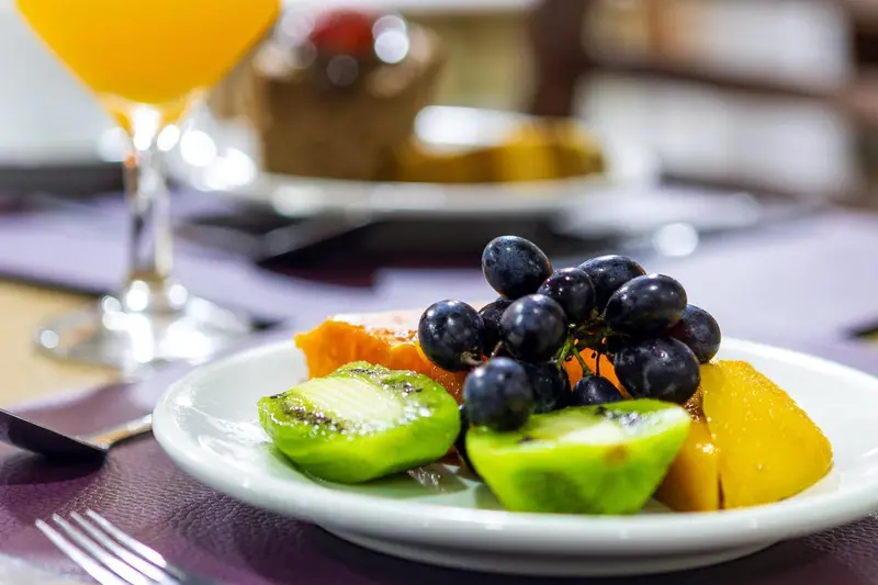 Une assiette de fruits frais et un verre de jus d'orange sont présentés sur une table.