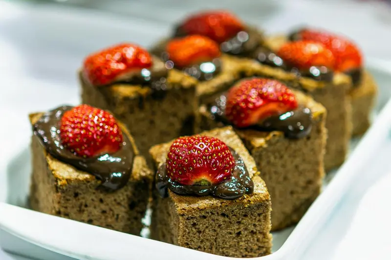 Des parts de gâteau au chocolat décorées de fraises fraîches et d'un glaçage brillant sont présentées sur un plat blanc.