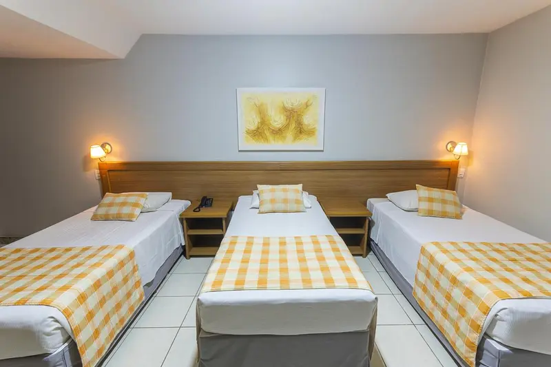 Trois lits simples avec couvertures à motifs dans une chambre lumineuse.