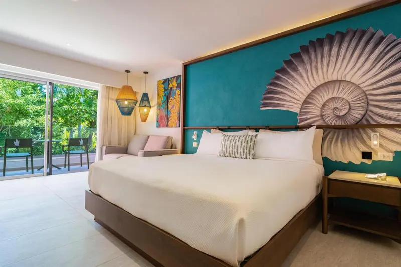 Chambre lumineuse avec un grand lit et un canapé face à une baie vitrée.