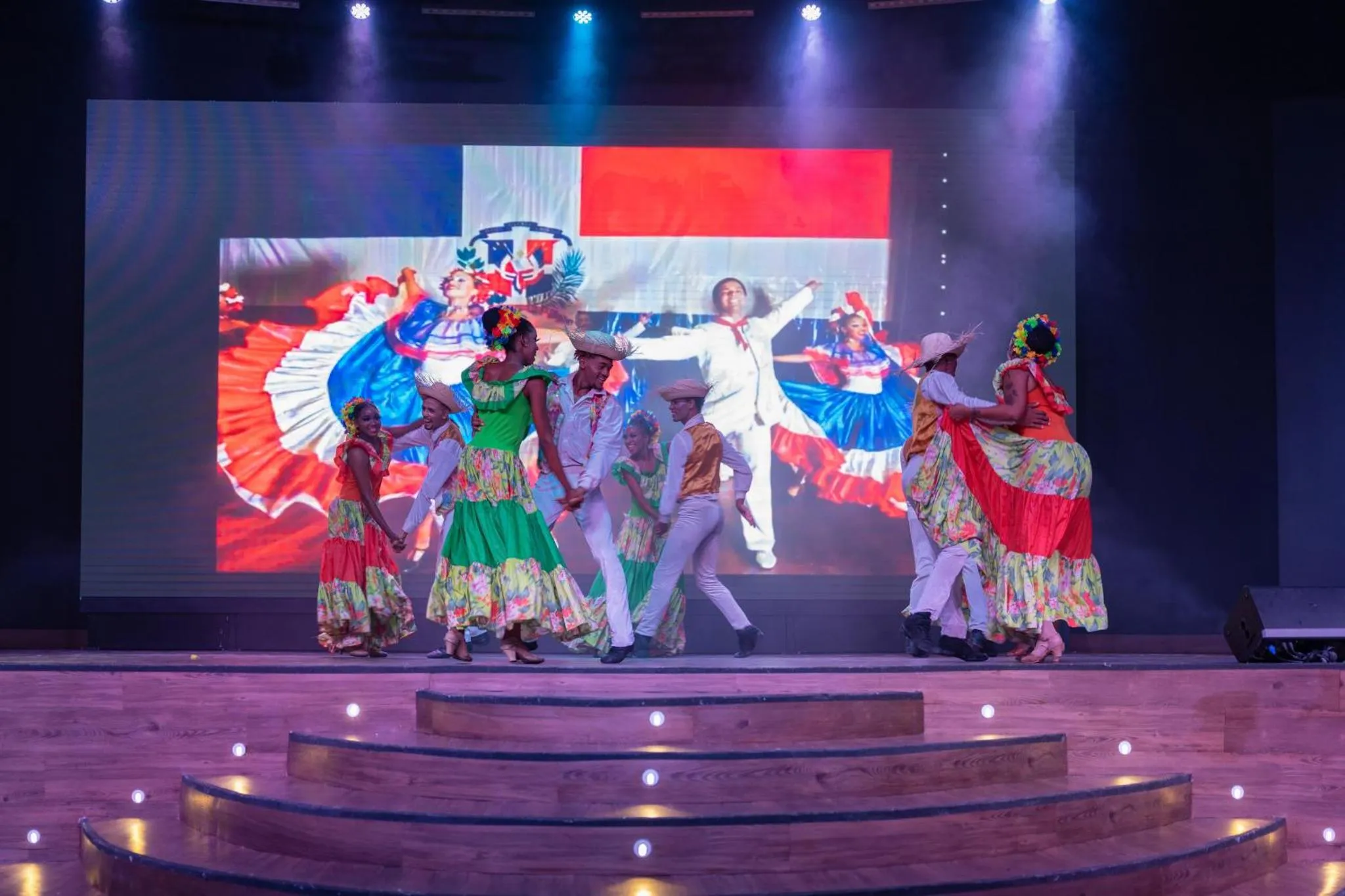 Groupe de danseurs en costumes traditionnels sur une scène illuminée.