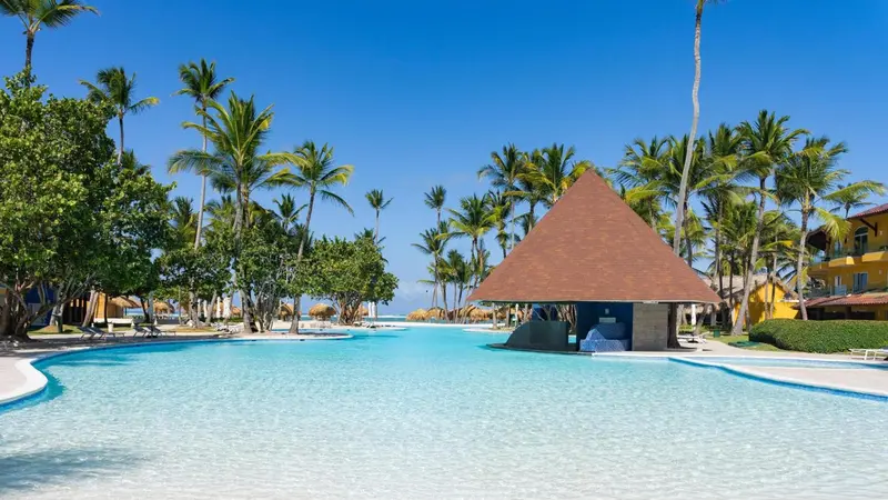 Une piscine turquoise bordée de palmiers et d'un kiosque à toit conique.