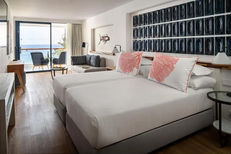 Chambre lumineuse avec un grand lit et un coin salon donnant sur la mer.