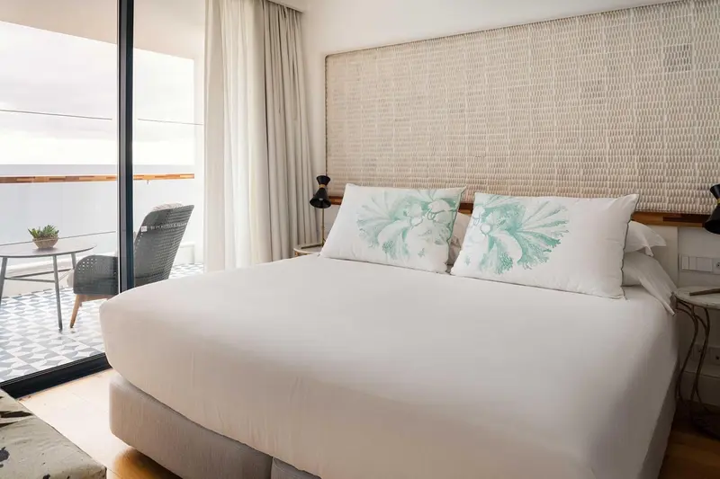 Une chambre lumineuse avec un grand lit et un accès à un balcon.