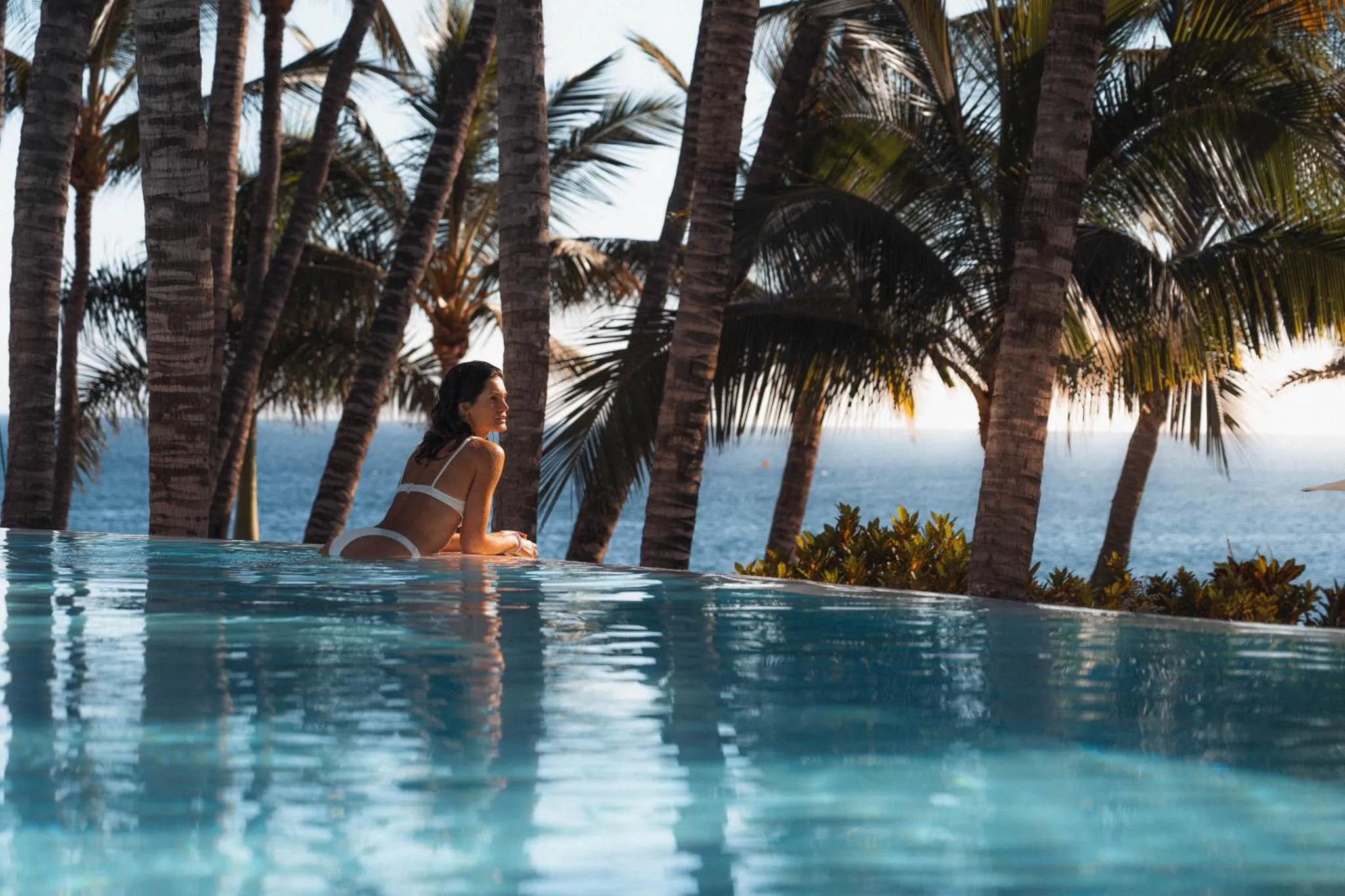Une femme se détend au bord d'une piscine à débordement face à la mer.