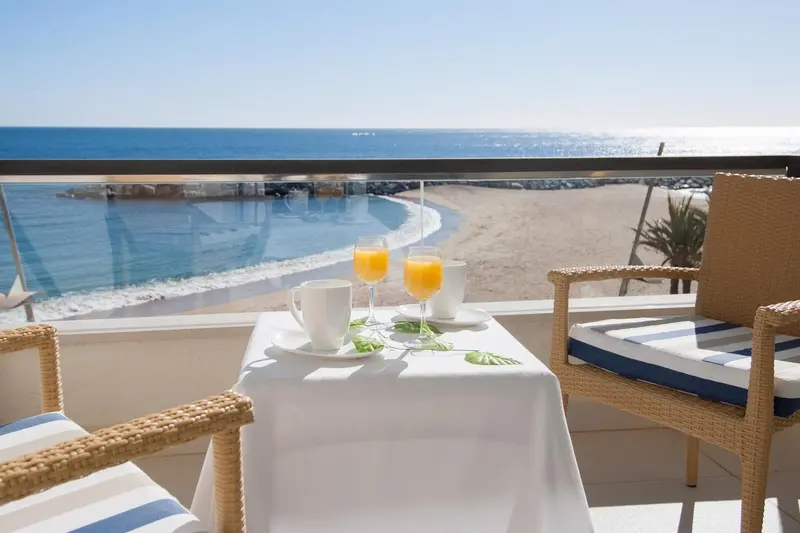 Une table avec des boissons est mise en scène sur une terrasse ensoleillée avec vue sur la mer.