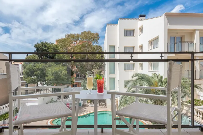 Deux fauteuils et une table avec des boissons sur un balcon ensoleillé.