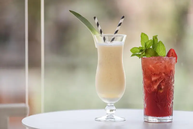 Deux cocktails colorés sont présentés sur une table blanche en extérieur.