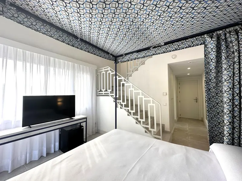 Une chambre lumineuse avec un lit blanc et un escalier menant à un autre niveau.
