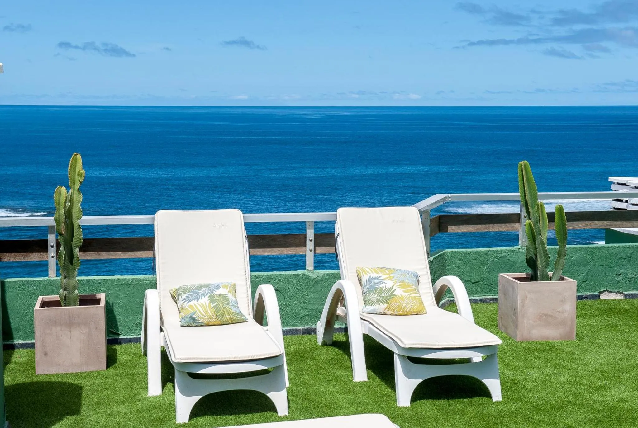 Deux transats blancs sur une terrasse verdoyante avec vue sur la mer.