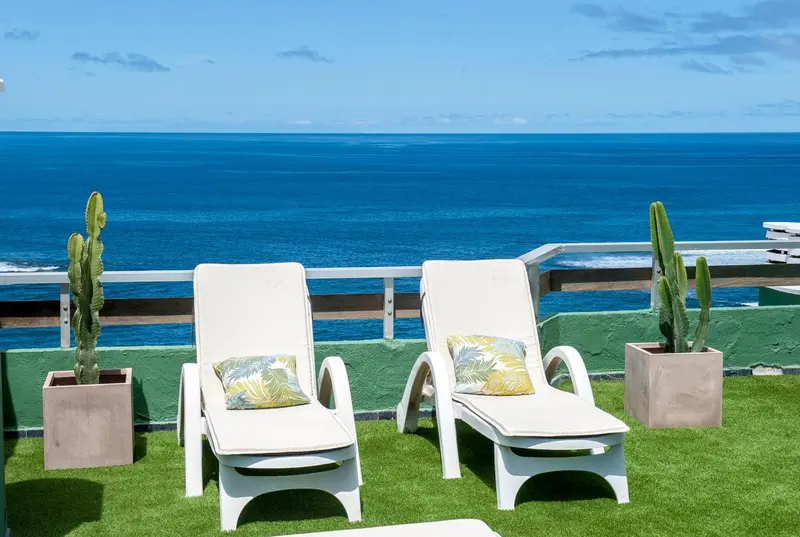 Deux transats blancs sur une terrasse verdoyante avec vue sur la mer.