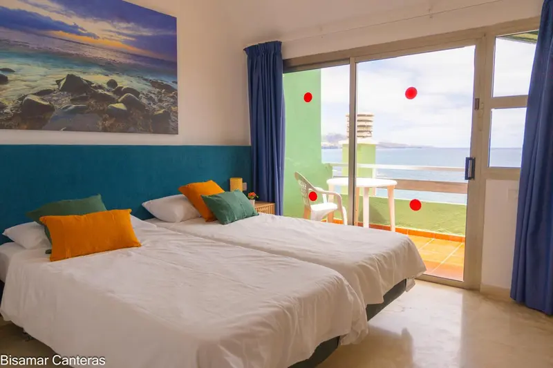 Une chambre lumineuse avec un lit blanc et une vue sur la mer depuis un balcon.