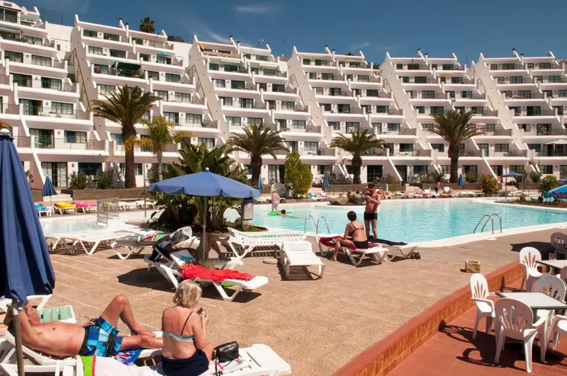 Vue d'une piscine ensoleillée devant un bâtiment blanc à plusieurs étages.
