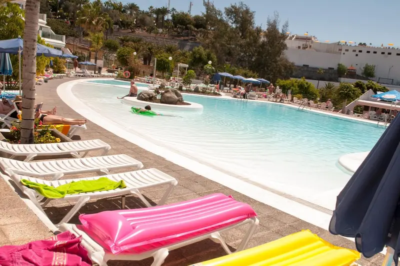 Transats colorés disposés autour d'une piscine ensoleillée.