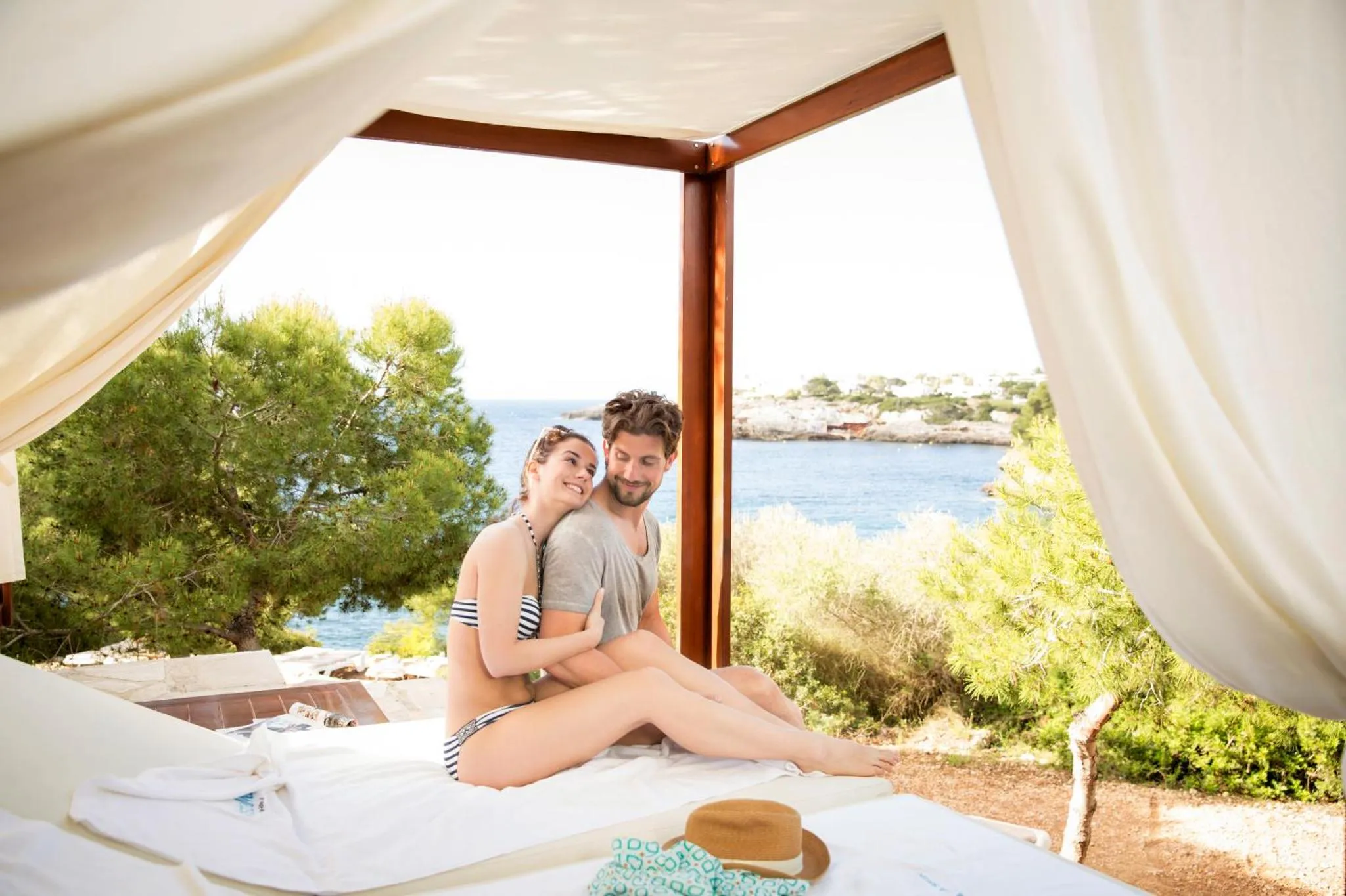 Un couple se détend sur un lit à baldaquin face à la mer.