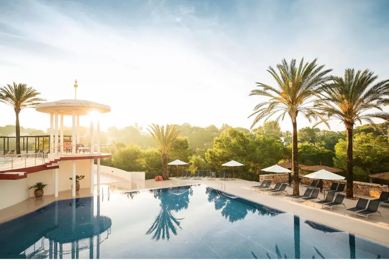 Une piscine bordée de transats sous les palmiers, avec un soleil éclatant.