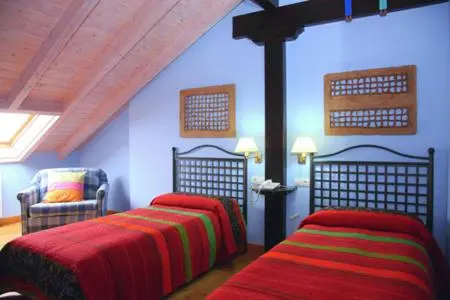 Chambre mansardée avec deux lits et un fauteuil.